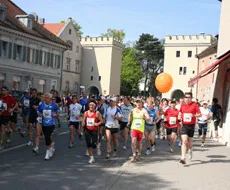 Eine Gruppe von Läufern in sportlicher Kleidung läuft durch eine Stadtstraße, wobei einige ein orangefarbenes Ballon halten.
