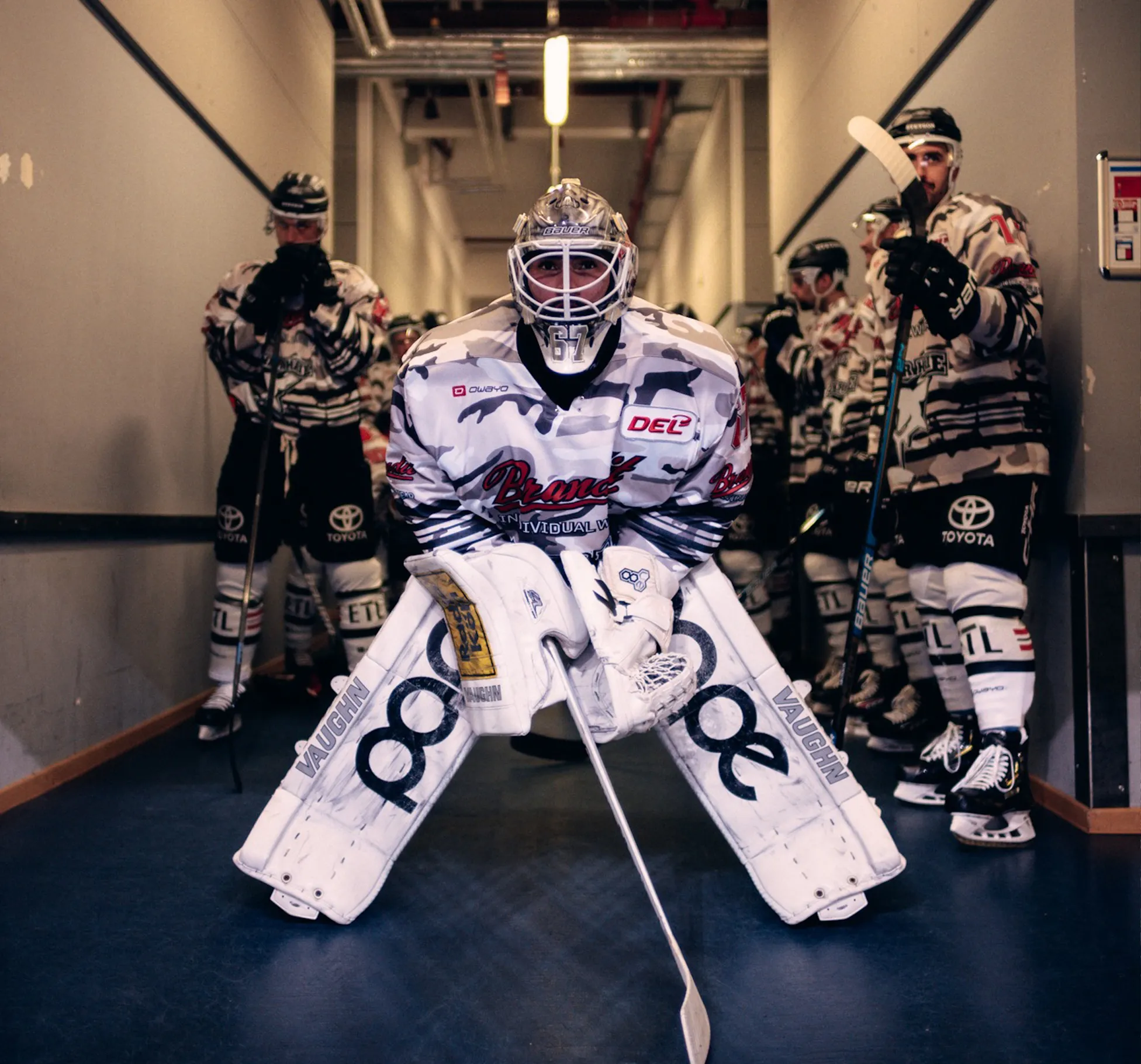 Ein Eishockeytorwart in einer auffälligen Uniform steht bereit, während andere Spieler hinter ihm warten.