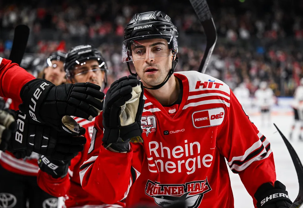 Ein Eishockeyspieler in einem roten Trikot mit schwarzen Handschuhen und einem Helm, der mit seinen Teamkollegen feiert.