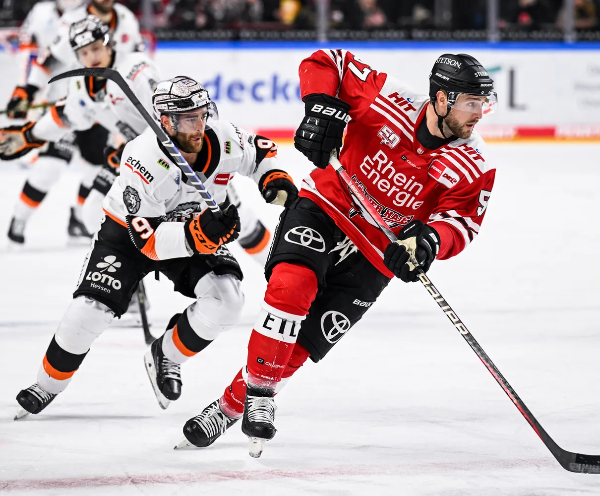 Zwei Eishockeyspieler auf dem Eis, einer in rotem Trikot und der andere in weißem Trikot mit orangefarbenen Akzenten.