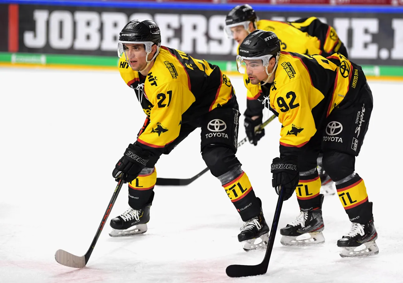Zwei Eishockeyspieler in gelb-schwarzen Trikots mit den Nummern 21 und 92 auf dem Eis, die sich auf das Spiel konzentrieren.
