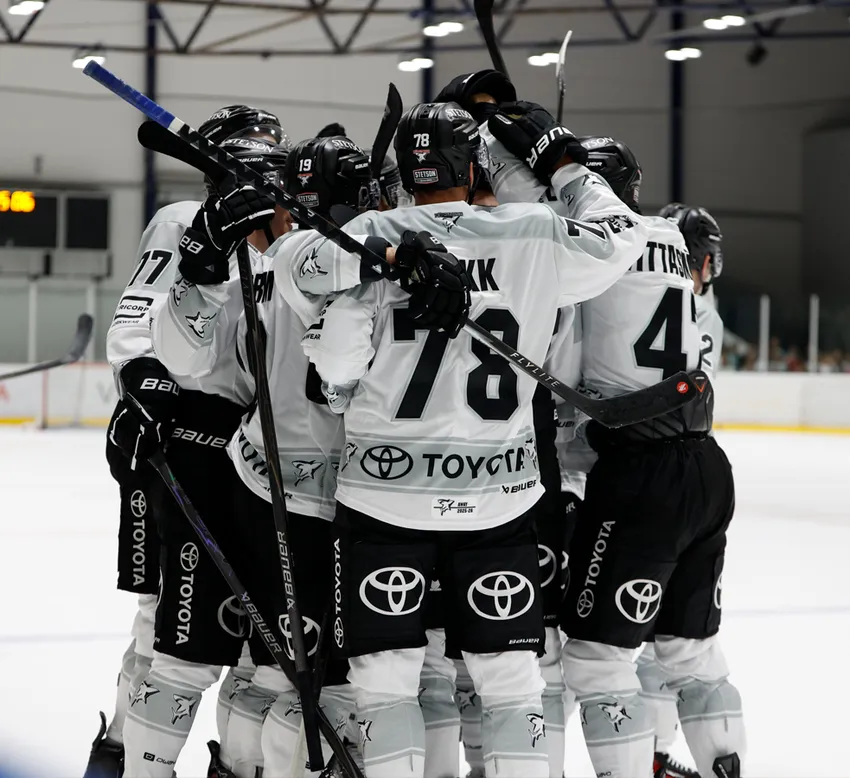Eishockeyspieler in weißen Trikots mit schwarzen Nummern und dem Toyota-Logo feiern auf dem Eis.