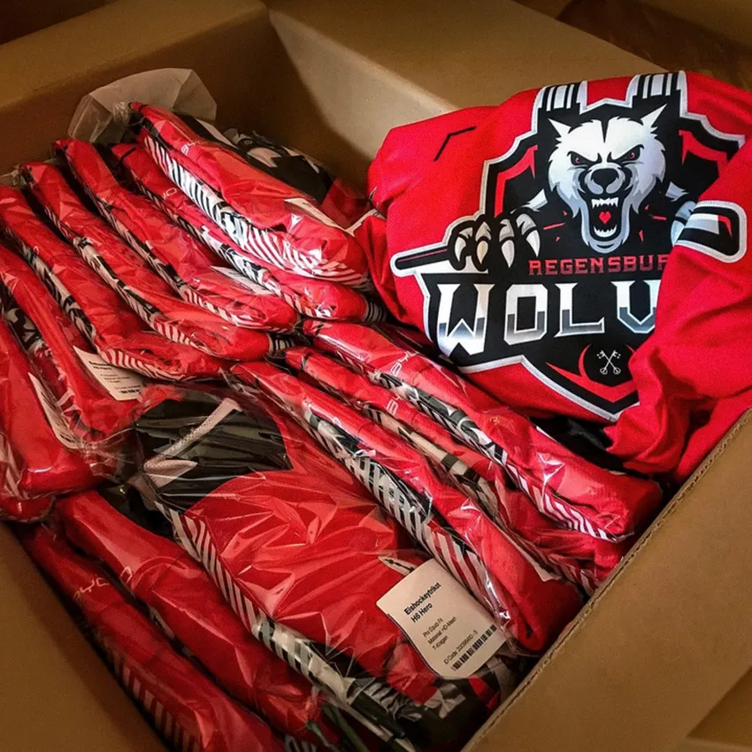 Ein Karton voller roter Sportbekleidung mit einem Wolf-Logo und verschiedenen Kleidungsstücken, die in durchsichtige Verpackungen gehüllt sind.
