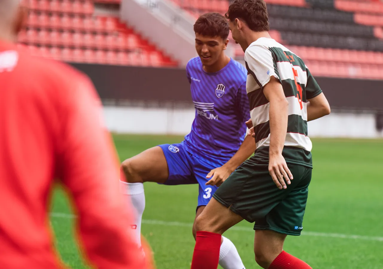Zwei Fußballspieler in action auf dem Spielfeld, einer trägt ein blaues Trikot, der andere ein gestreiftes Trikot in grün und weiß.