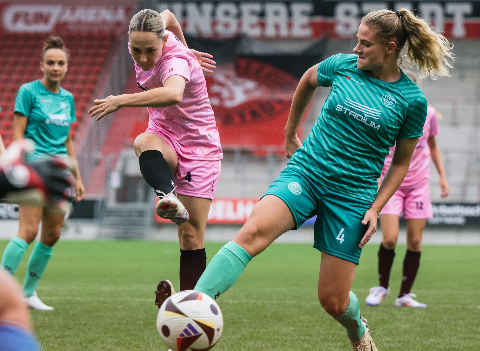 Zwei Frauen in farbigen Sporttrikots spielen Fußball auf einem Rasenfeld.