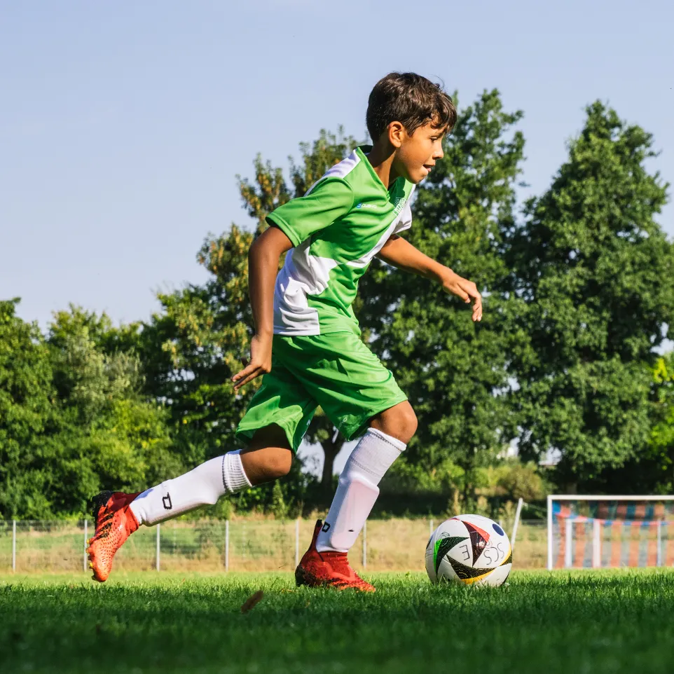 Ein junger Fußballspieler in grün-weißer Sportkleidung läuft auf einem Fußballfeld.