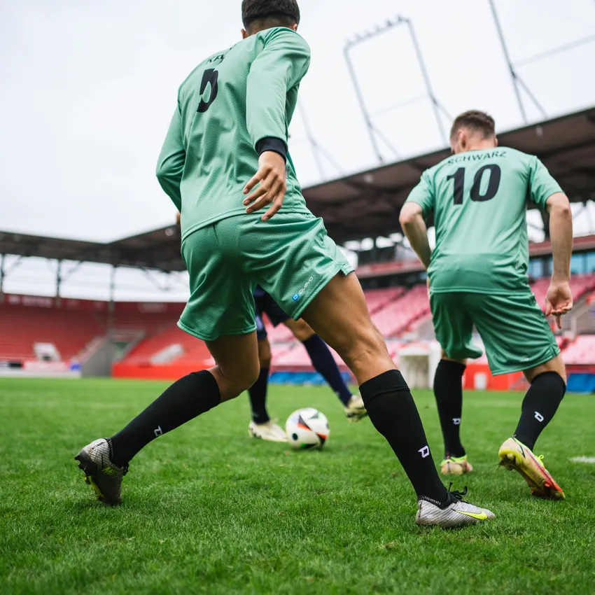 Zwei Spieler in grünen Fußballtrikots und schwarzen Socken, die auf einem Spielfeld in einem Stadion agieren.