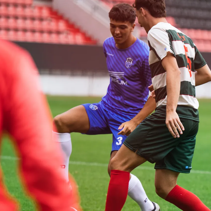 Zwei Fußballspieler in action auf dem Spielfeld, einer trägt ein blaues Trikot und der andere ein gestreiftes Trikot in grün und rot.
