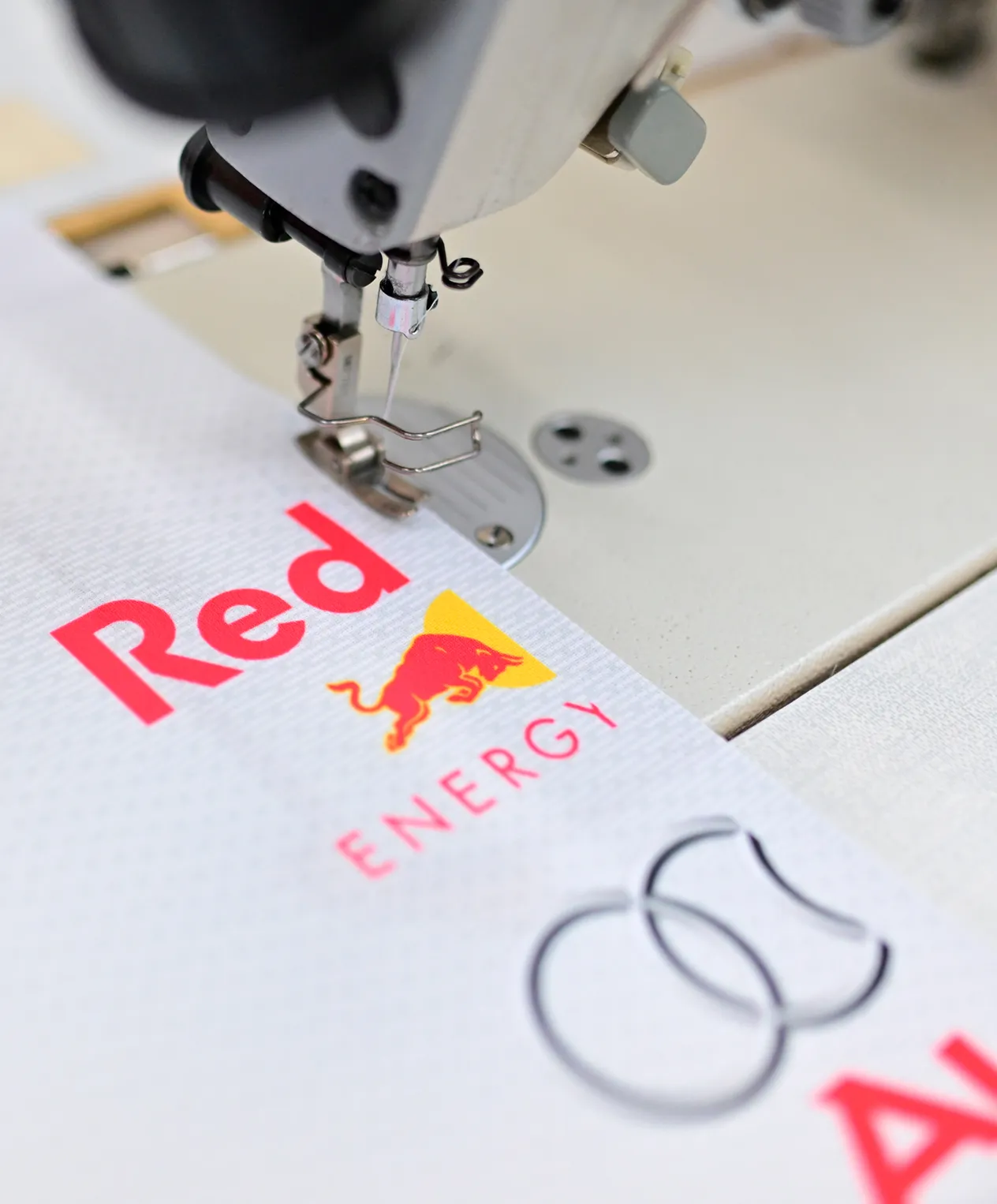 Eine Nähmaschine näht ein weißes Sportbekleidungsstück mit dem Red Bull Energy-Logo.