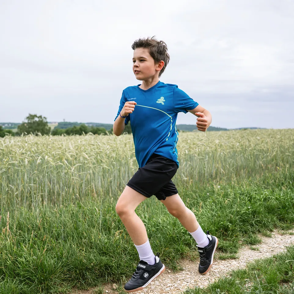 Ein Junge läuft auf einem Feldweg, gekleidet in einem blauen Sporttrikot und schwarzen Shorts.
