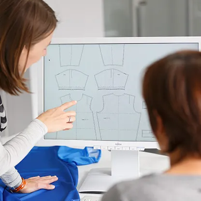 Zwei Personen betrachten auf einem Computerbildschirm digitale Schnittmuster für Sportbekleidung, während eine Person auf den Bildschirm zeigt.