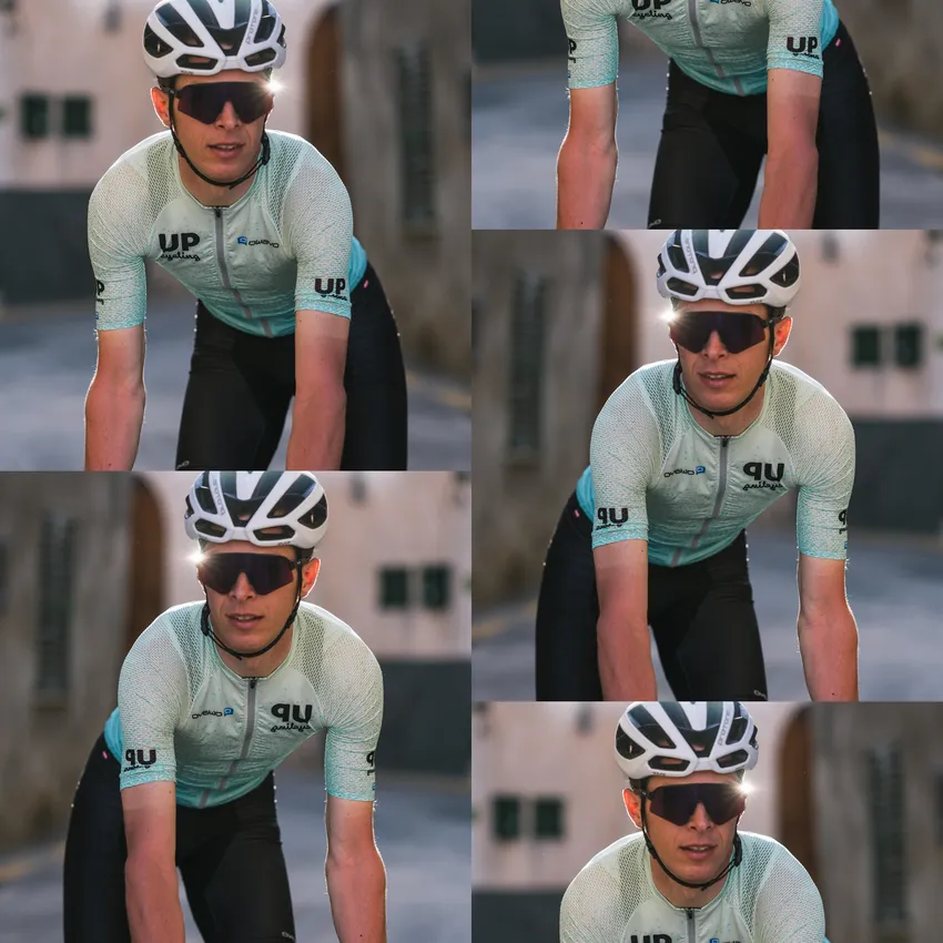 Ein Radfahrer in einem hellblauen Trikot mit kurzen Ärmeln und einer Sonnenbrille, der auf einem Fahrrad in einer urbanen Umgebung fährt.